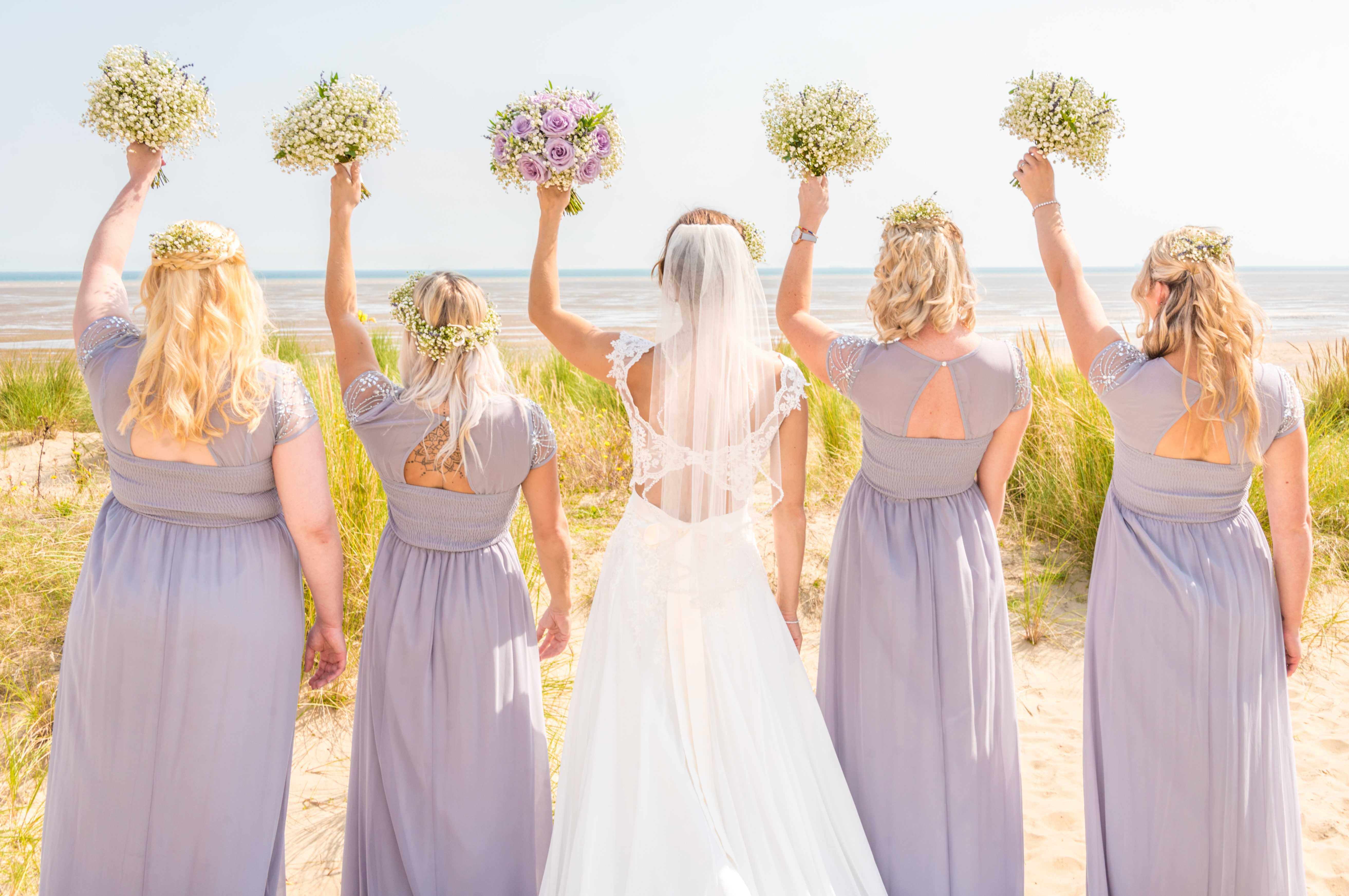 The bridal party hold 5 bouquets aloft at a Kent Wedding